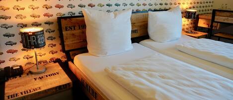 A neatly made bed with white linens, a headboard with a vintage design, and a wall decorated with a pattern of vintage cars.