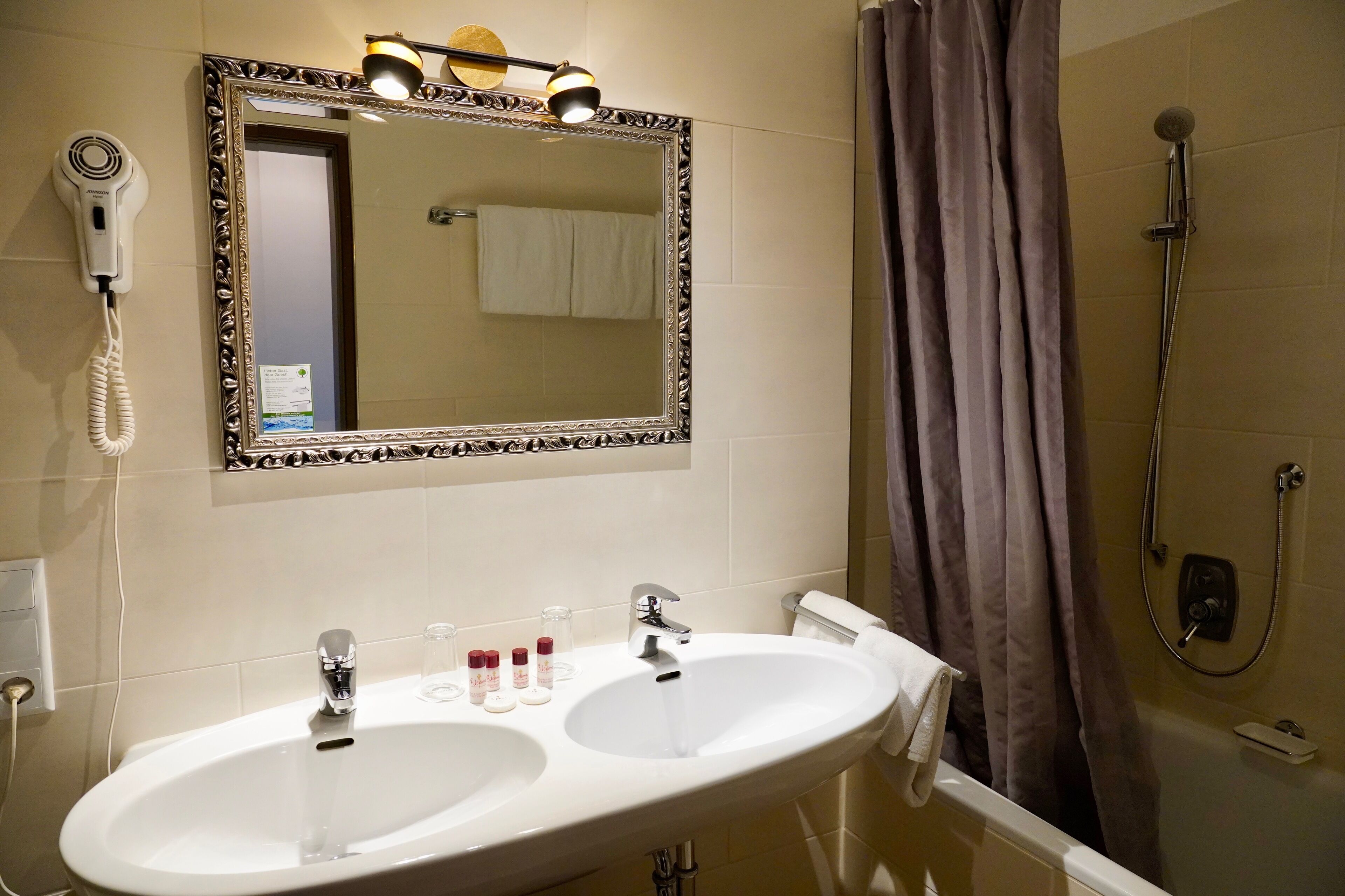 Une salle de bain avec deux lavabos, un miroir, un sèche-cheveux et une douche.