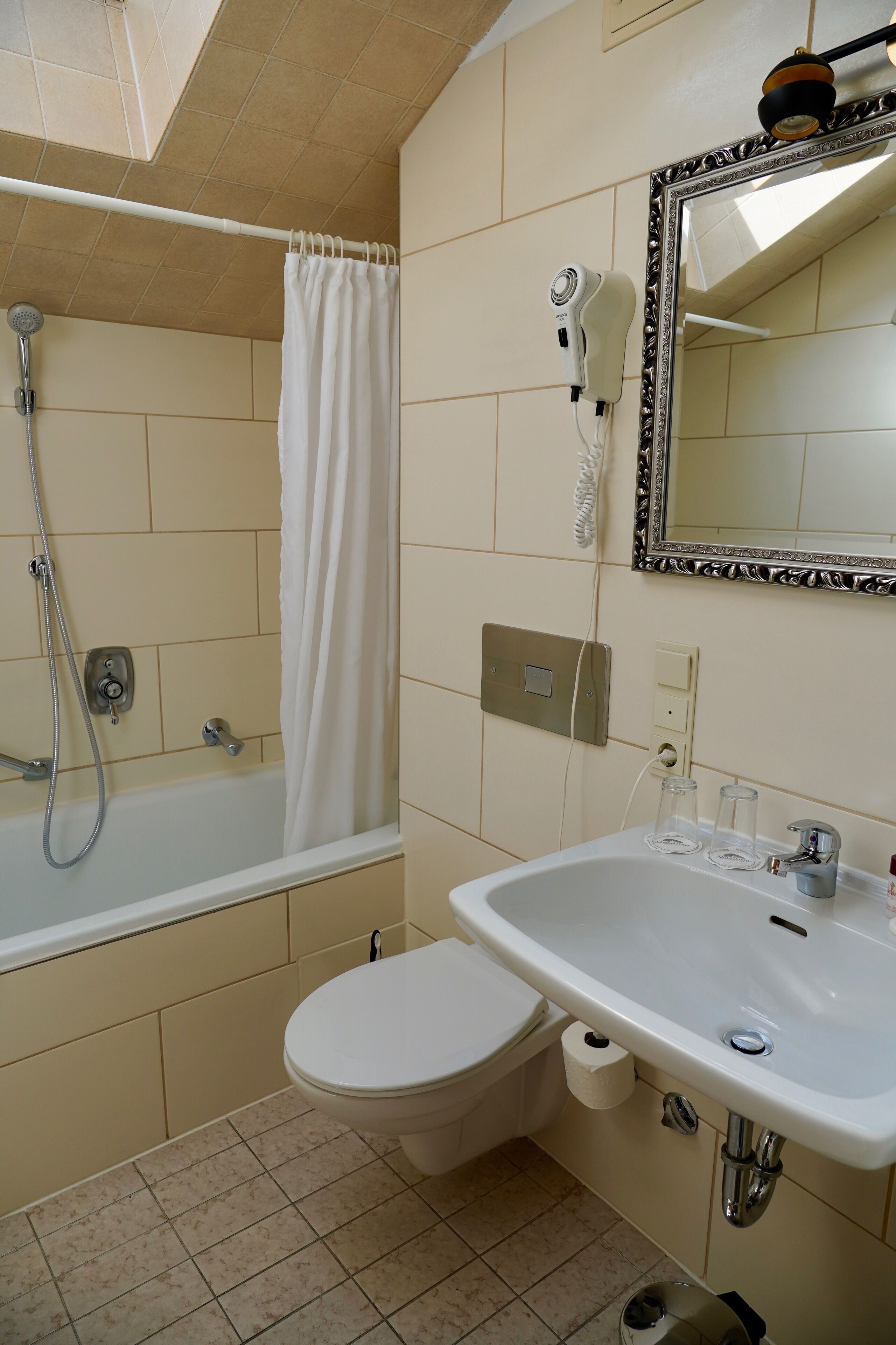 Un baño con bañera, inodoro, lavamanos y un secador de pelo en la pared.