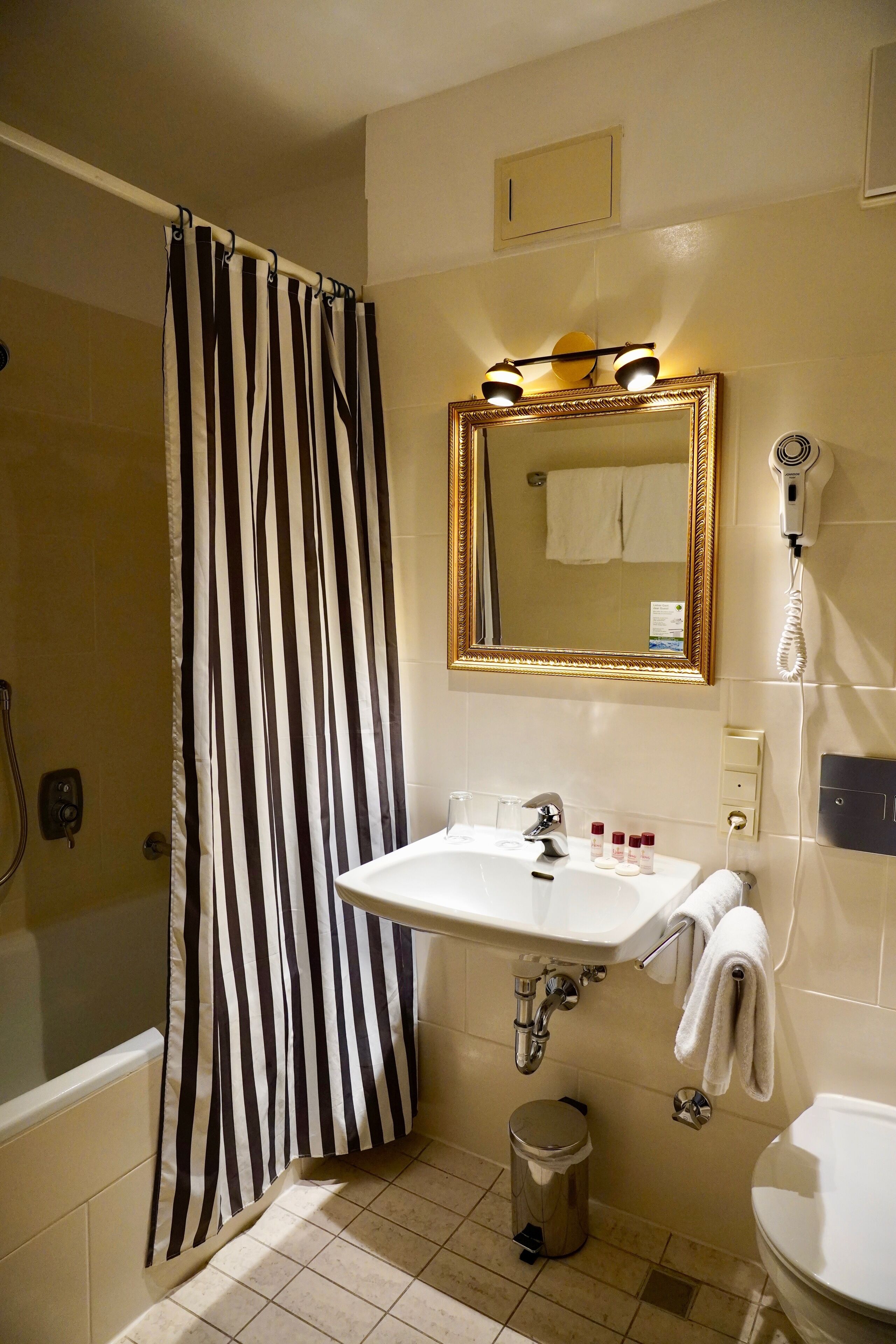 A bathroom with a shower curtain, a sink with a mirror, a hairdryer, and a toilet.