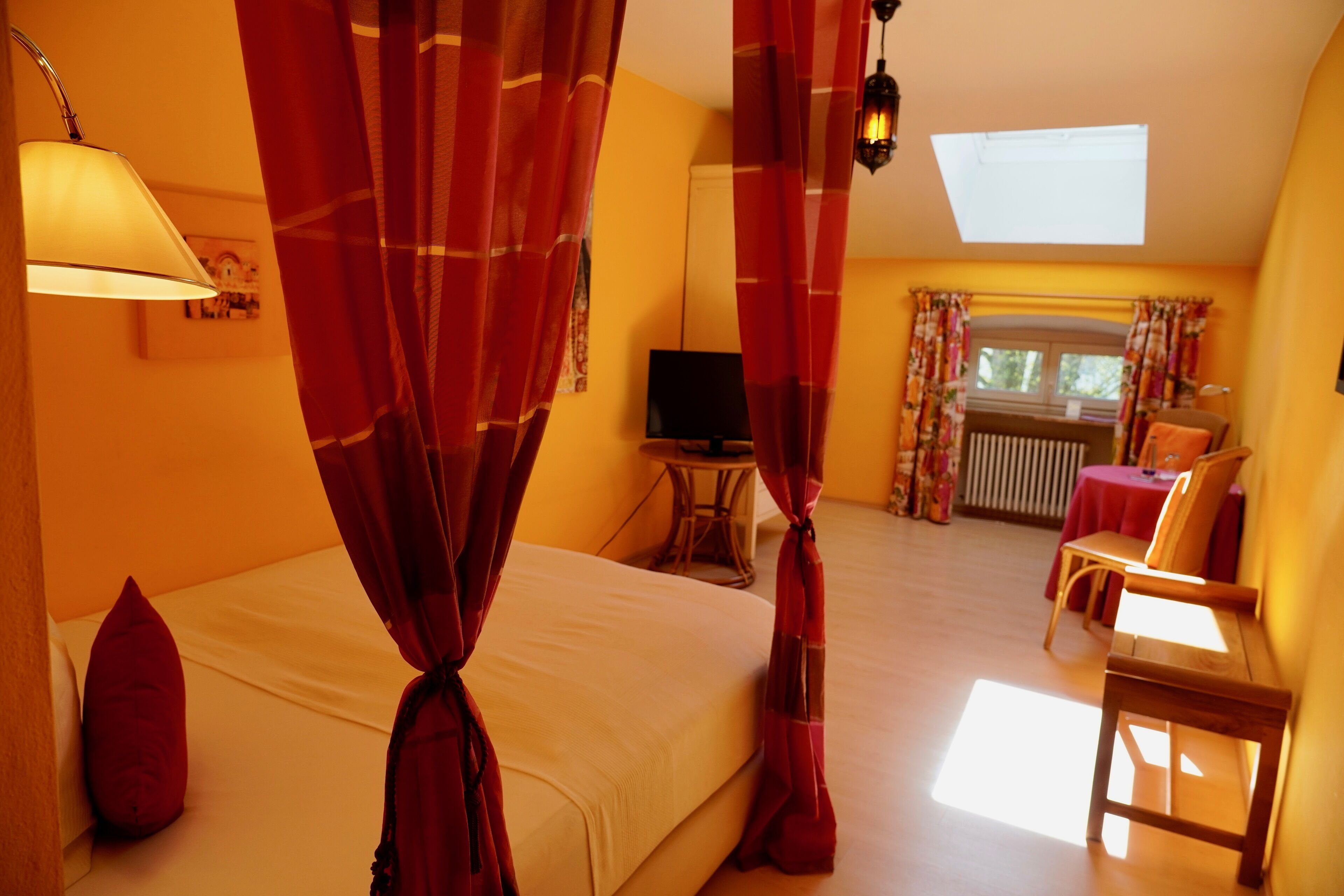 A bedroom with a bed, curtains, a television, a chair, and a table.