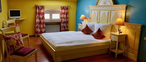 A bedroom with a bed, bedside tables, a chair, a desk, a TV, and a window with curtains.