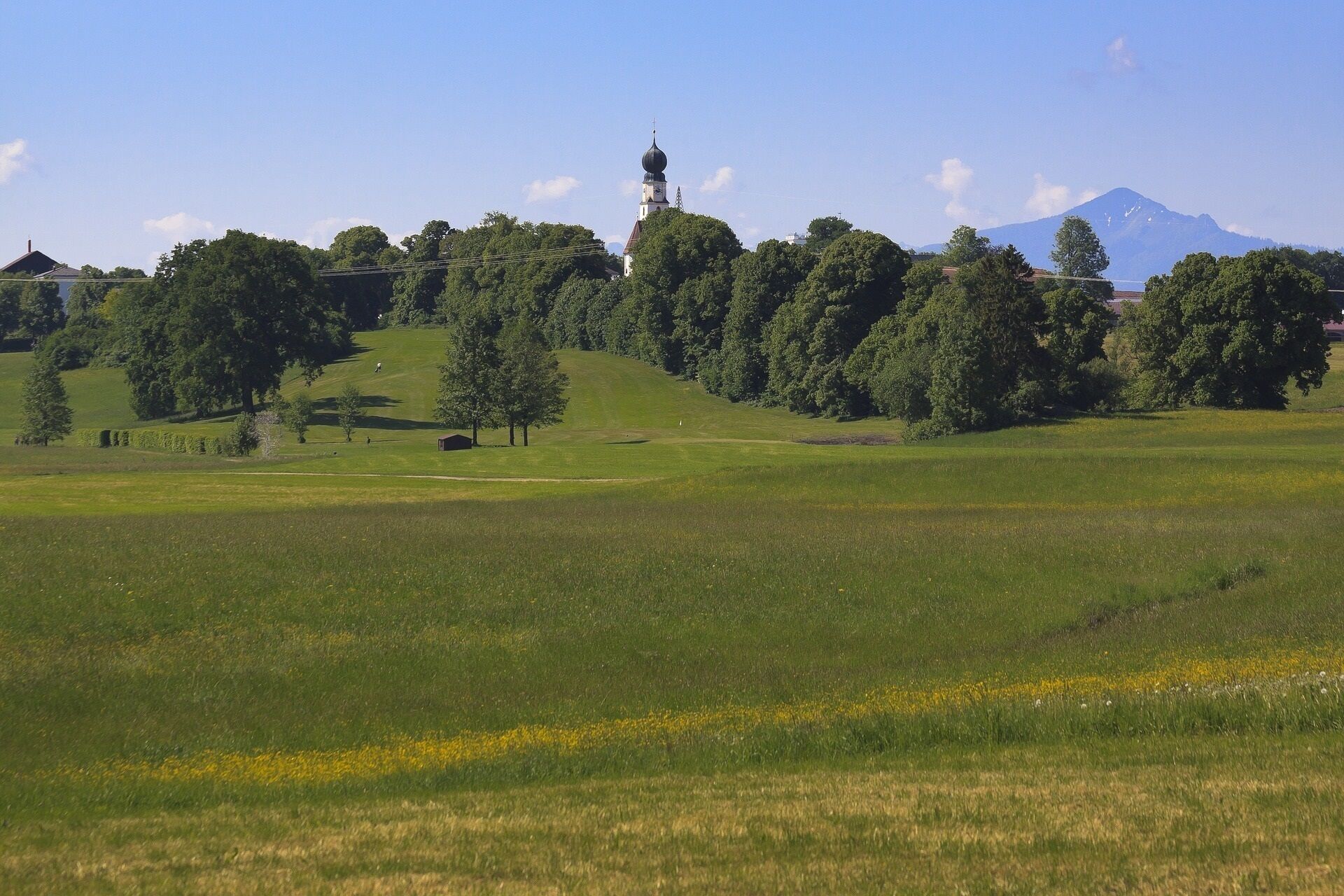 A grassy field with a church and a mountain in the background.