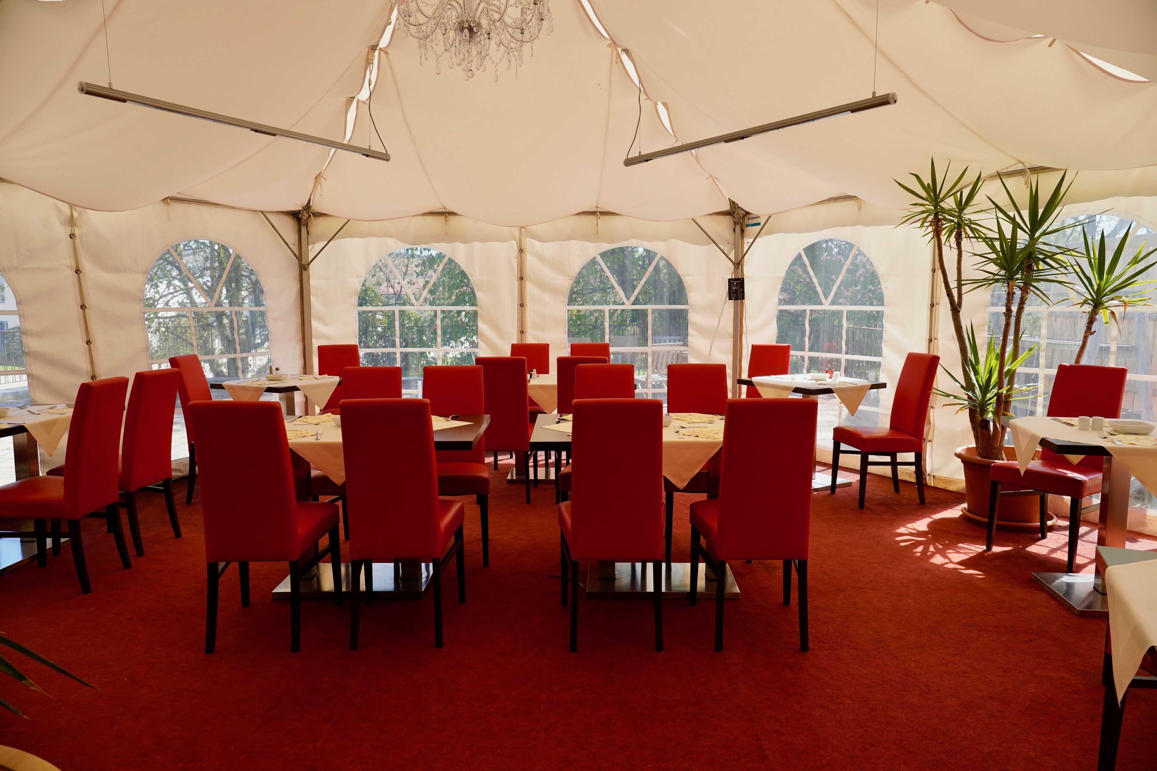 A tented dining area with red chairs and tables, large arched windows, and a chandelier.