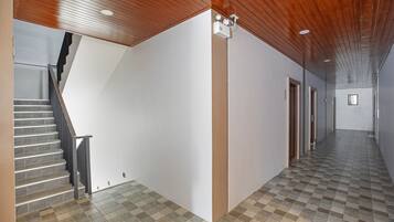 Een gang met een trap, houten plafond en betegelde vloer.