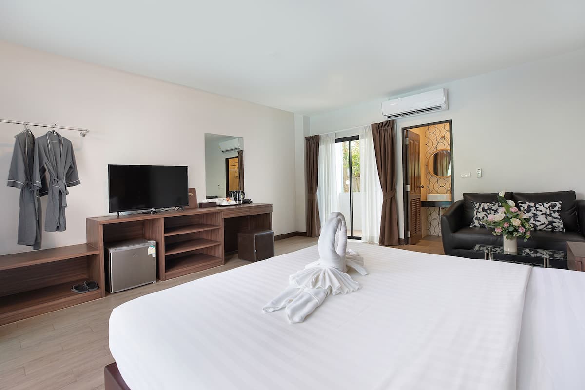 Una habitación de hotel con una cama grande, televisor, escritorio, refrigerador pequeño y zona de estar con sofá y mesa de centro.