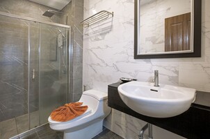 Un baño moderno con ducha envuelta en cristal, inodoro blanco, lavamanos blanco y salpicadero de mármol.