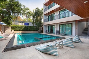 A modern pool area with lounge chairs and a multi-story building with balconies.