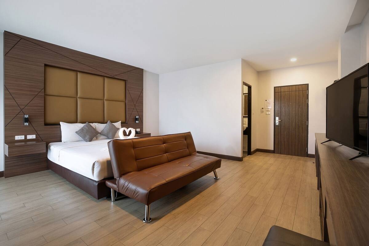 Una habitación de hotel moderna con una cama grande, un sofá de cuero marrón, un televisor de pantalla plana y un armario de madera.