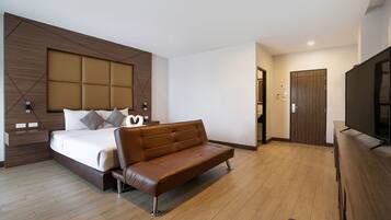 A modern hotel room with a large bed, a brown leather sofa, a flat-screen TV, and a wooden wardrobe.