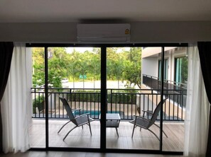 Un balcon avec deux chaises et une table, un appareil de climatisation installé au-dessus, et une vue sur une piscine et la verdure.