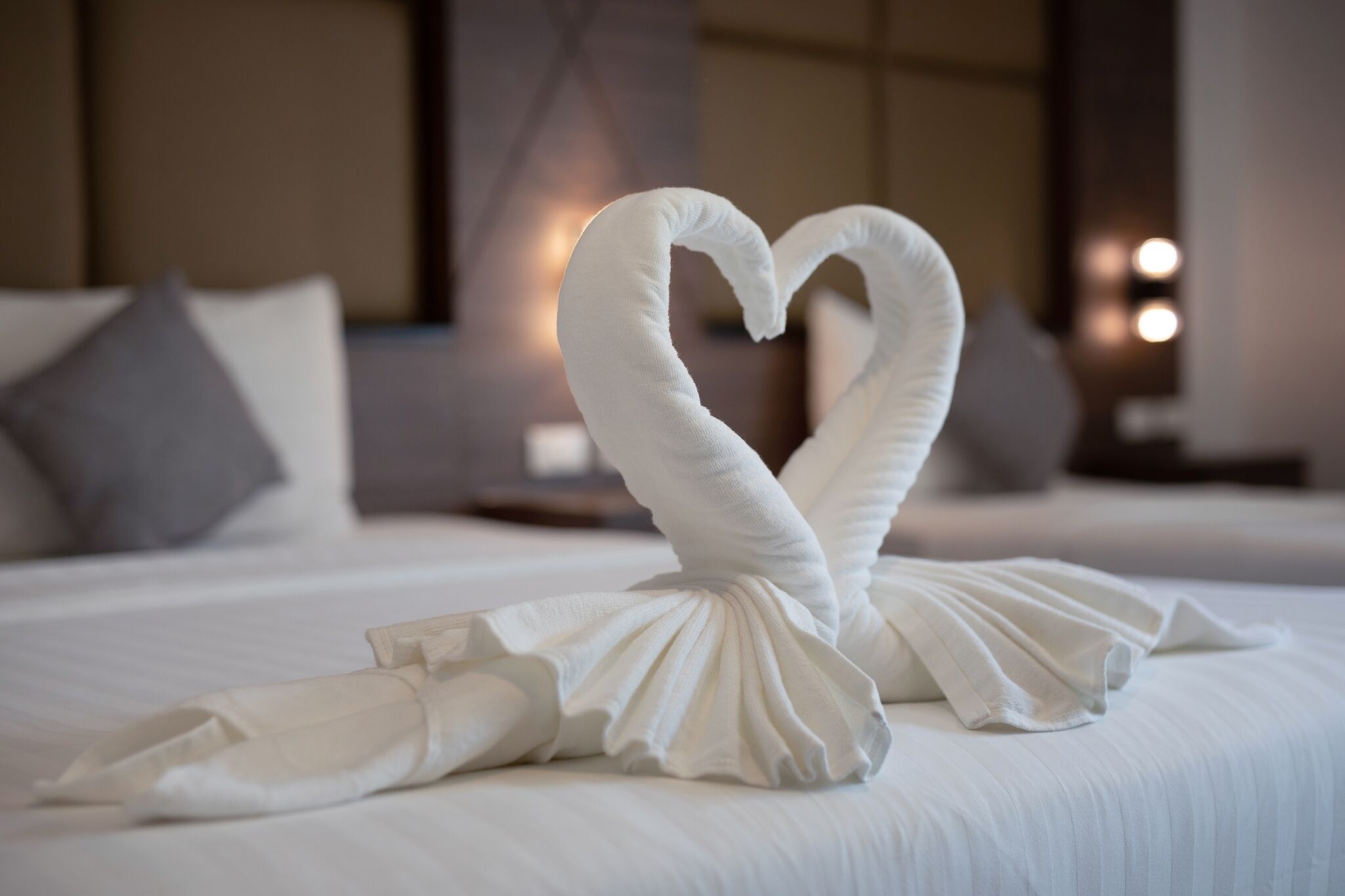 Una cama bien hecha con una toalla dispuesta en forma de corazón.