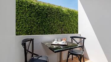 Un balcón con una mesa y dos sillas, un muro de seto verde y un cielo despejado.