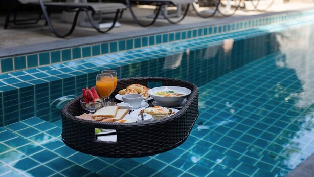 Un plateau de petit-déjeuner avec divers aliments et boissons, posé sur une table au bord de la piscine.