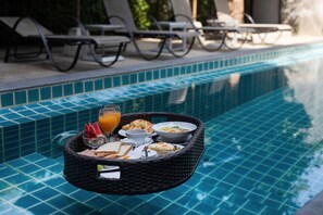 Una bandeja de desayuno con diversos alimentos y bebidas sobre una mesa junto a la piscina.