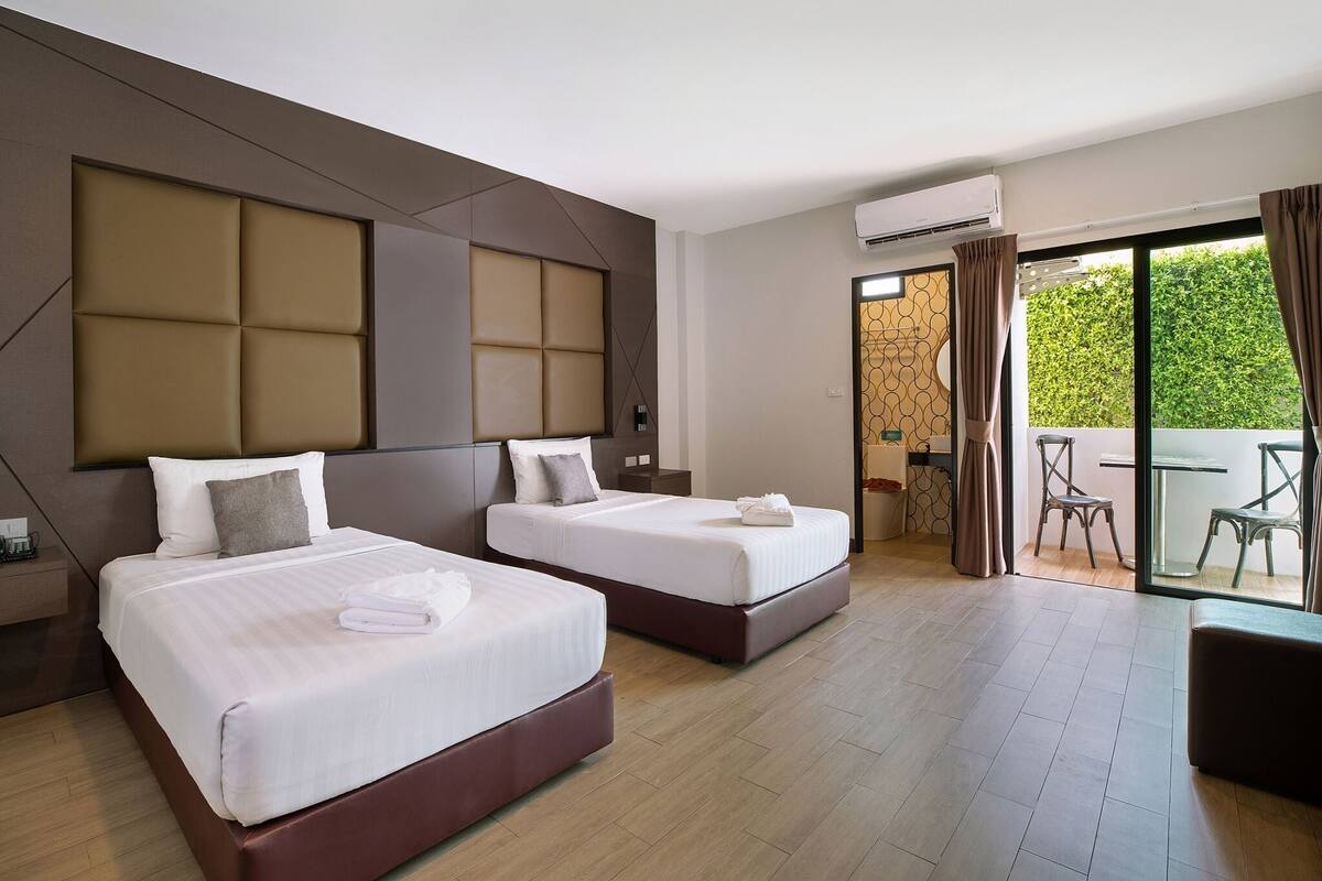 Habitación de hotel con dos camas, un balcón con mesa y sillas, y un equipo de aire acondicionado.