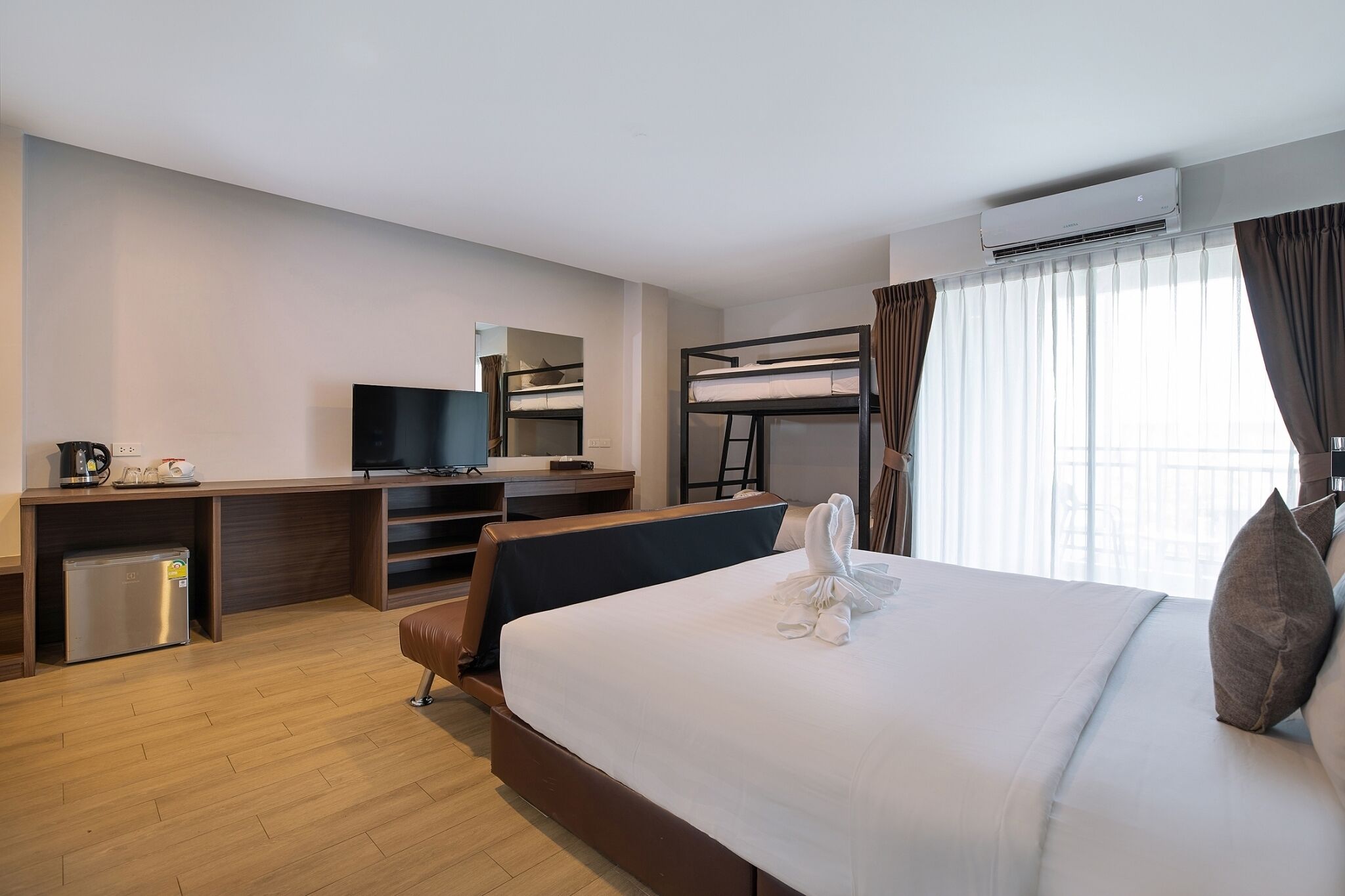 Habitación de hotel con cama, escritorio con televisor, mini refrigerador, literas y aire acondicionado.