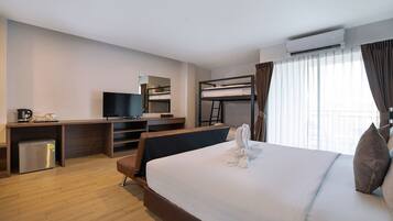 Habitación de hotel con cama, escritorio con televisor, mini refrigerador, literas y aire acondicionado.
