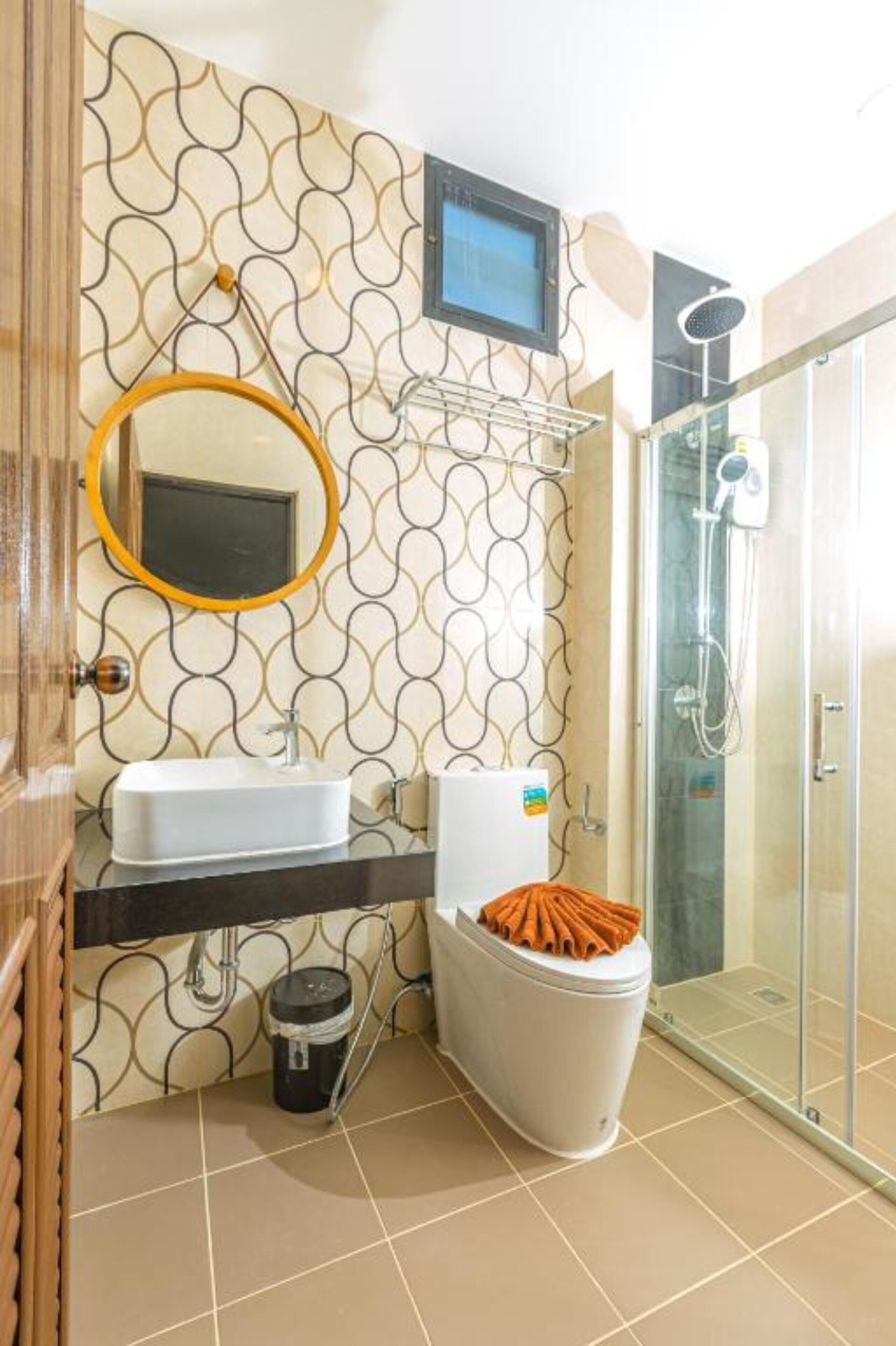 A bathroom with a patterned wall, a white sink, a toilet, and a glass shower enclosure.