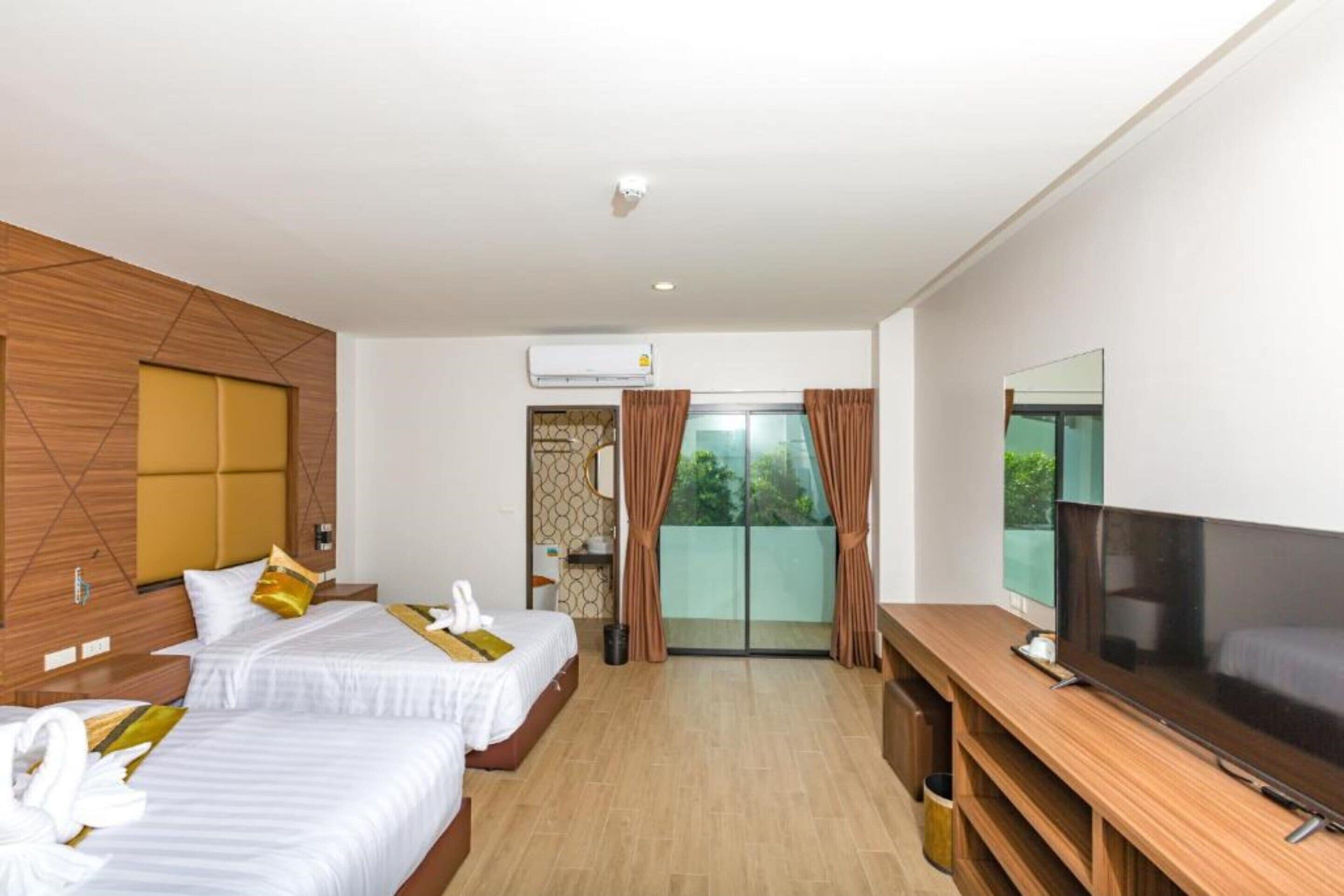 Quarto de hotel com duas camas, televisão, varanda com cortinas e ar condicionado.