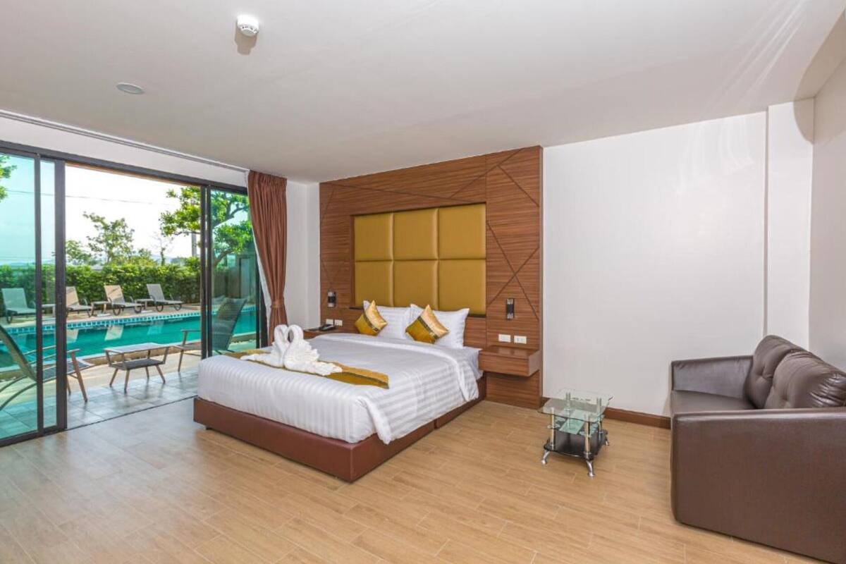 Una habitación de hotel moderna con una cama grande, un balcón con cerramiento de vidrio y una piscina, y un sofá de cuero.
