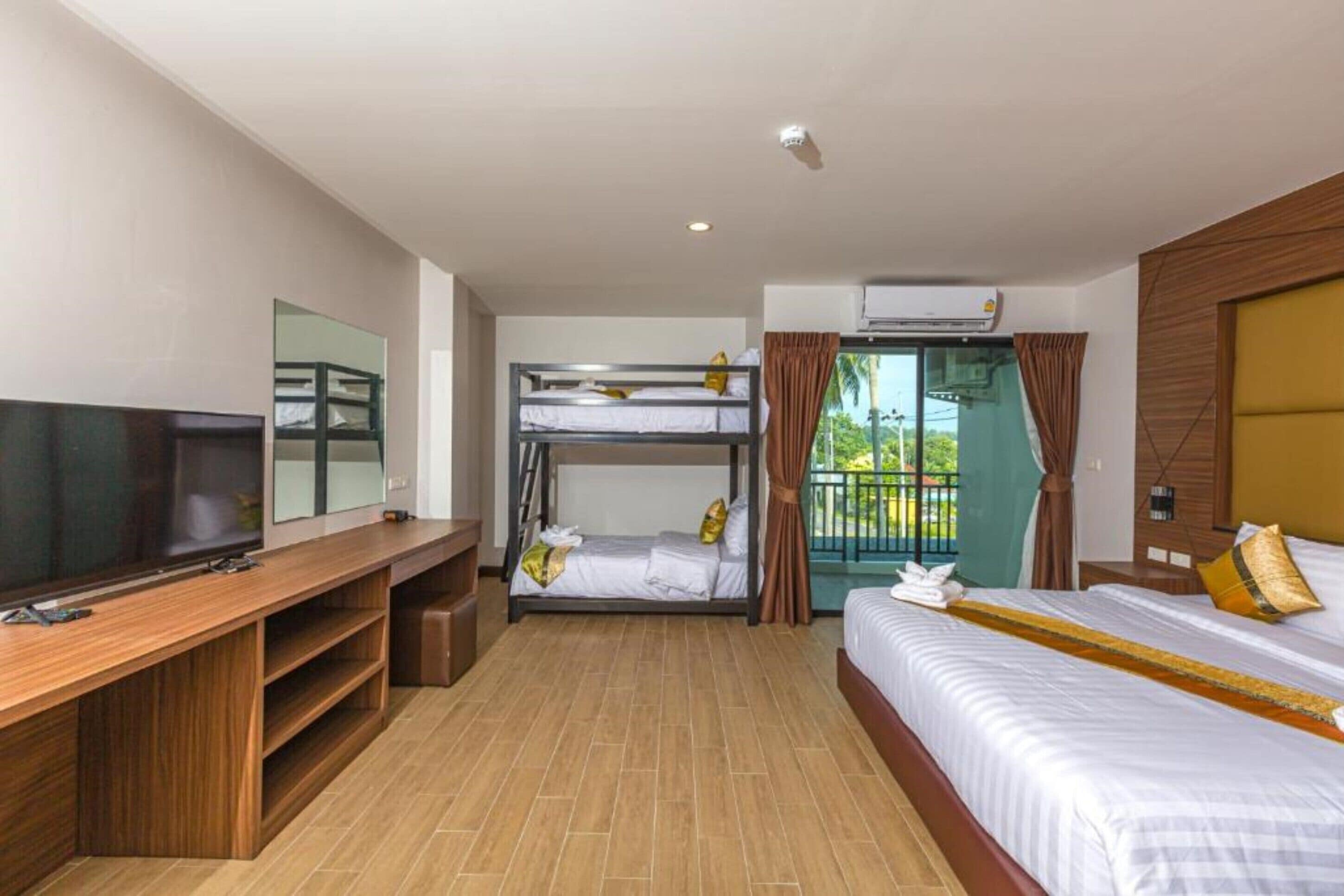 A hotel room with a bunk bed, a TV, a wooden desk, and a balcony with curtains.