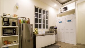 A compact kitchen with a stainless steel refrigerator, a microwave, and a coffee maker. There is a window above the sink, and a white door with blue signage. - Hualien Bird's House Hostel (Hualien City)