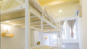 A bunk bed room with a wooden floor, a small shelf with a lamp, and a window with curtains. - Hualien Bird's House Hostel (Hualien City)