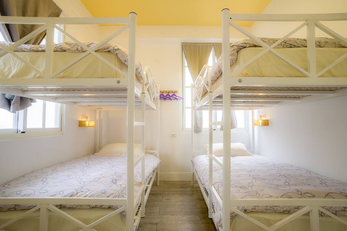 Une chambre avec des lits superposés, une fenêtre avec des rideaux et des lampes fixées au mur.