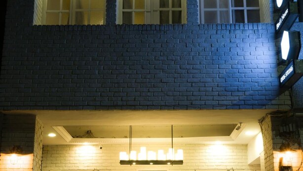 A building with a brick facade, three illuminated windows, a white door with glass panels, and a bicycle parked outside. - Hualien Bird's House Hostel (Hualien City)