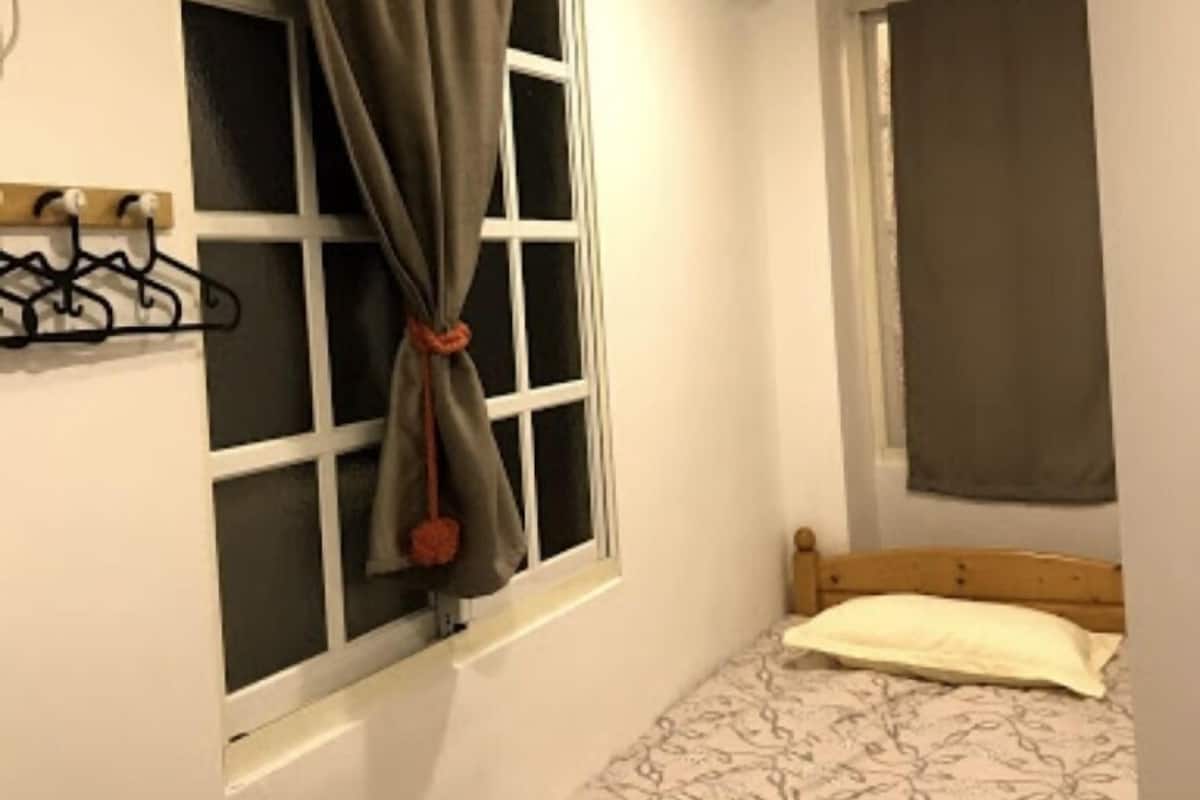 Une petite chambre avec un lit simple, une fenêtre avec des rideaux et un porte-manteau fixé au mur.