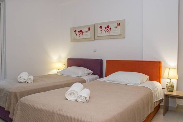 A hotel room with two beds, each with a rolled towel, a nightstand with a lamp, and two framed pictures on the wall.