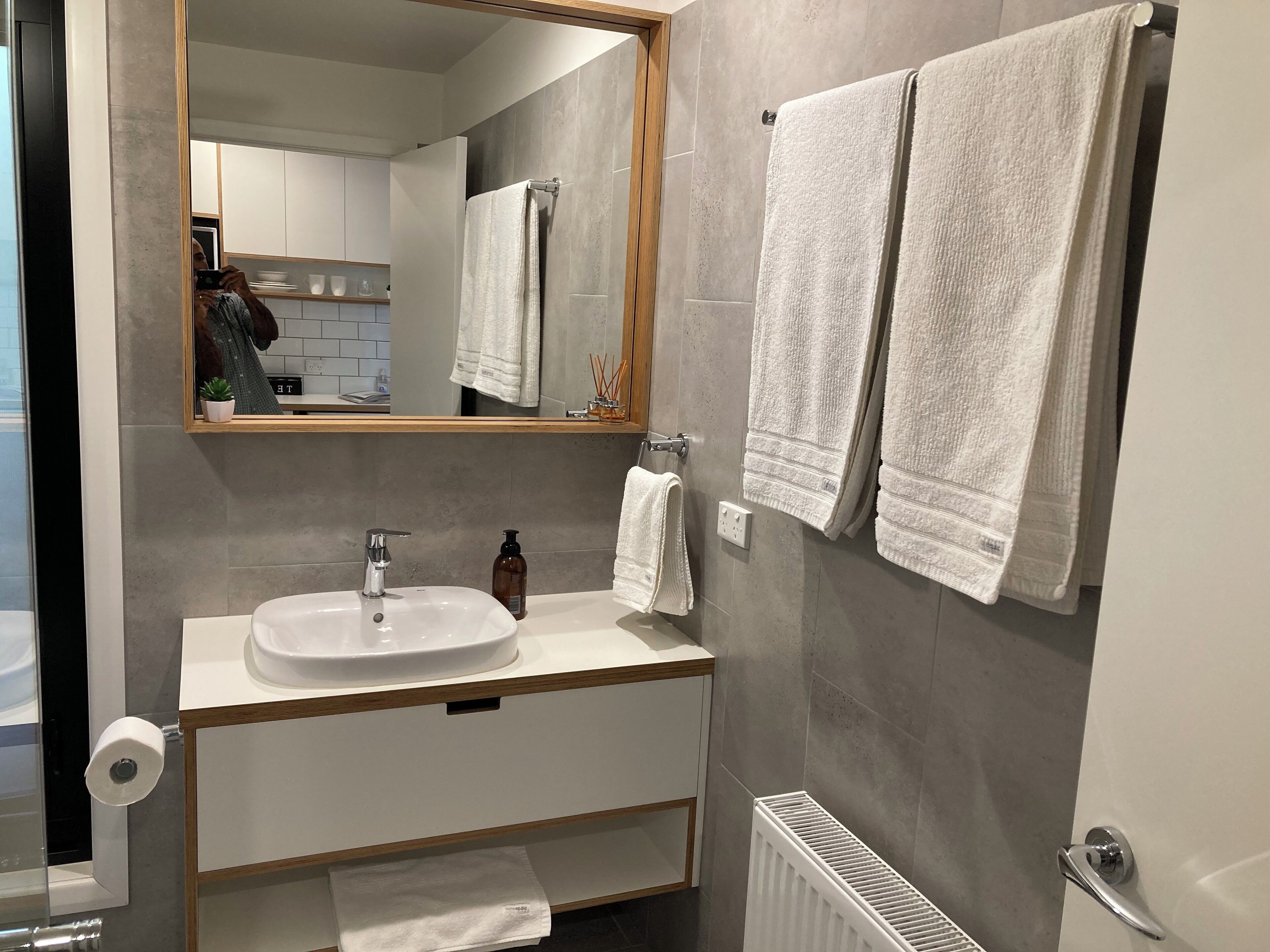 Un baño moderno con un lavabo blanco, espejo y dos toallas colgadas en un perchero.