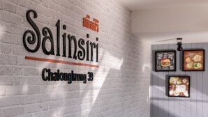 Une enseigne portant les noms « Salinsiri » et « Chalongkirung 39 », fixée sur un mur en briques blanches.