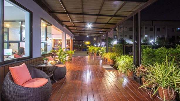 Un espace extérieur abrité, doté d’un plancher en bois, de meubles en osier et de plantes en pot.