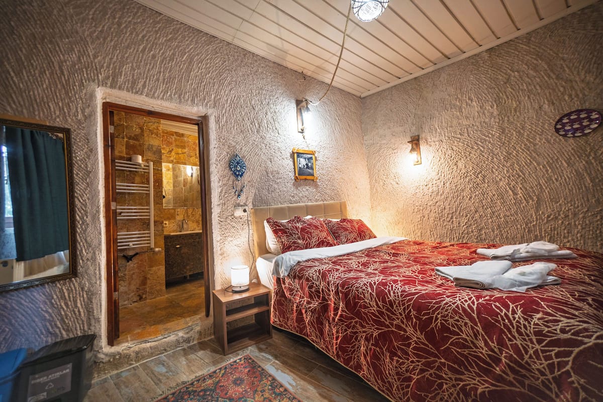 A bedroom with a bed, a nightstand, a wall-mounted light, a door leading to a bathroom, and a patterned rug.
