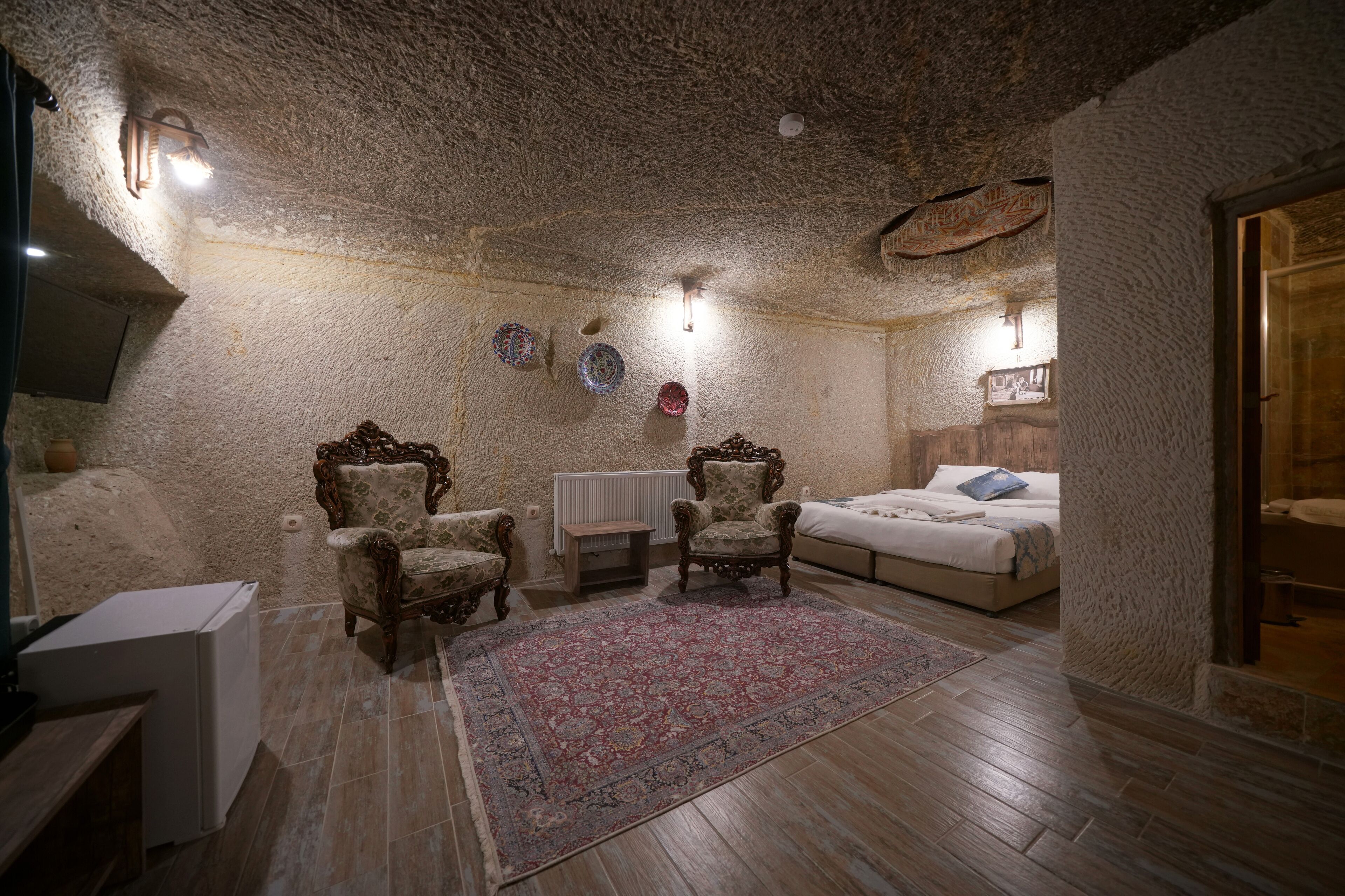 A cozy room with a stone ceiling, a bed, two ornate chairs, a small table, and a radiator.