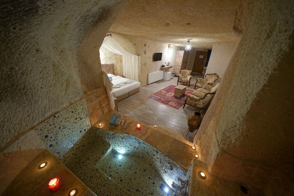 A cozy, stone-walled bedroom with a large bed, a sitting area with a chair, and a small bathroom.