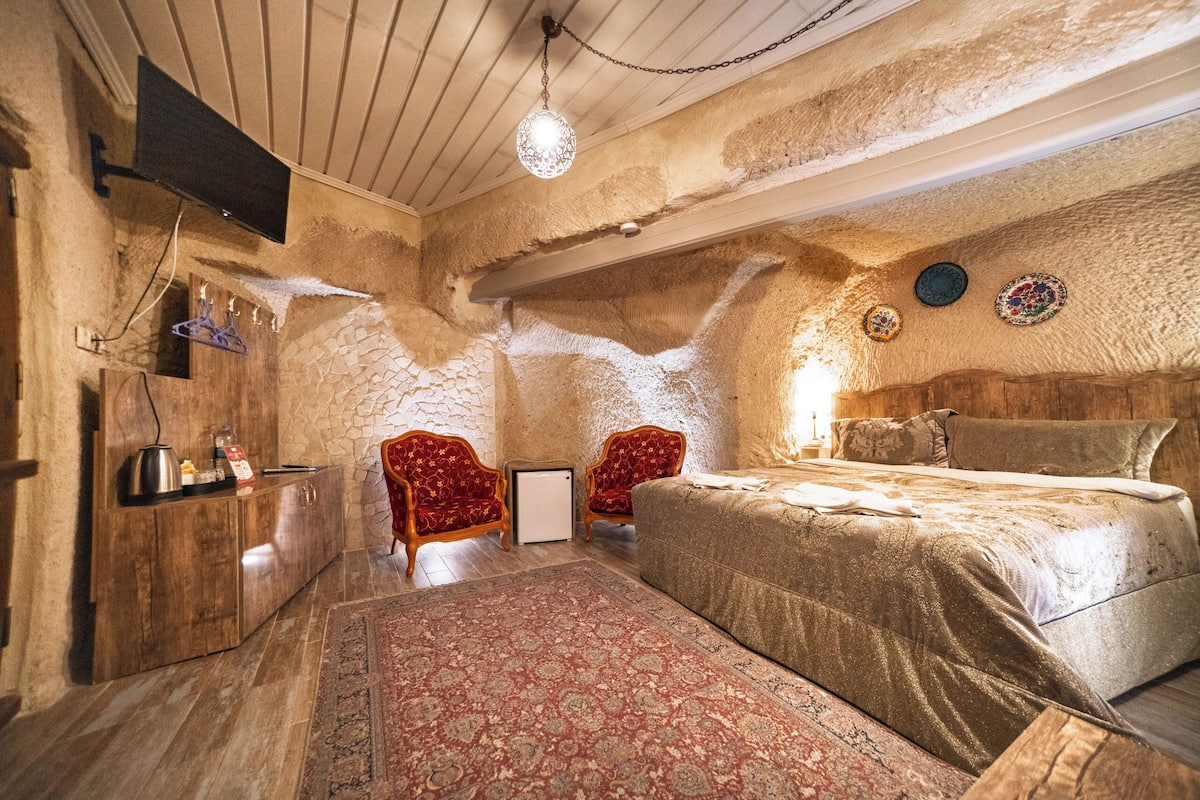 A bedroom with a bed, two red armchairs, a small table, a TV, and a decorative wall.
