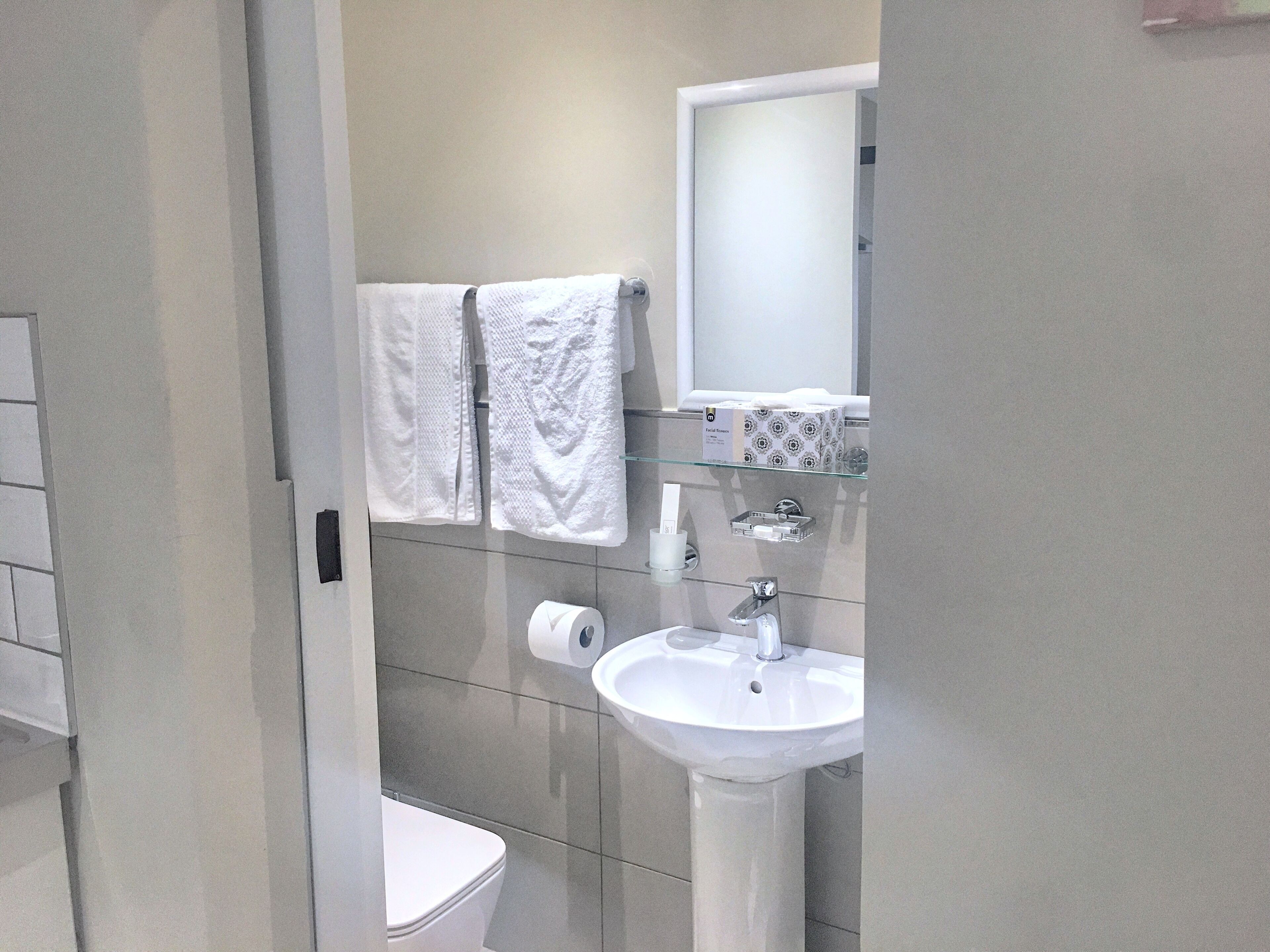 A modern bathroom with a white sink, a mirror, and two towels hanging on the wall.