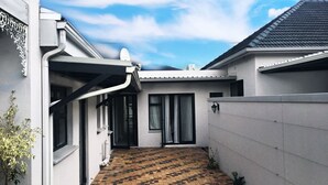 A narrow pathway leading to a building entrance with a patterned brick floor, a white exterior wall, and a black roof. - Selton Guest House (Cape Town)