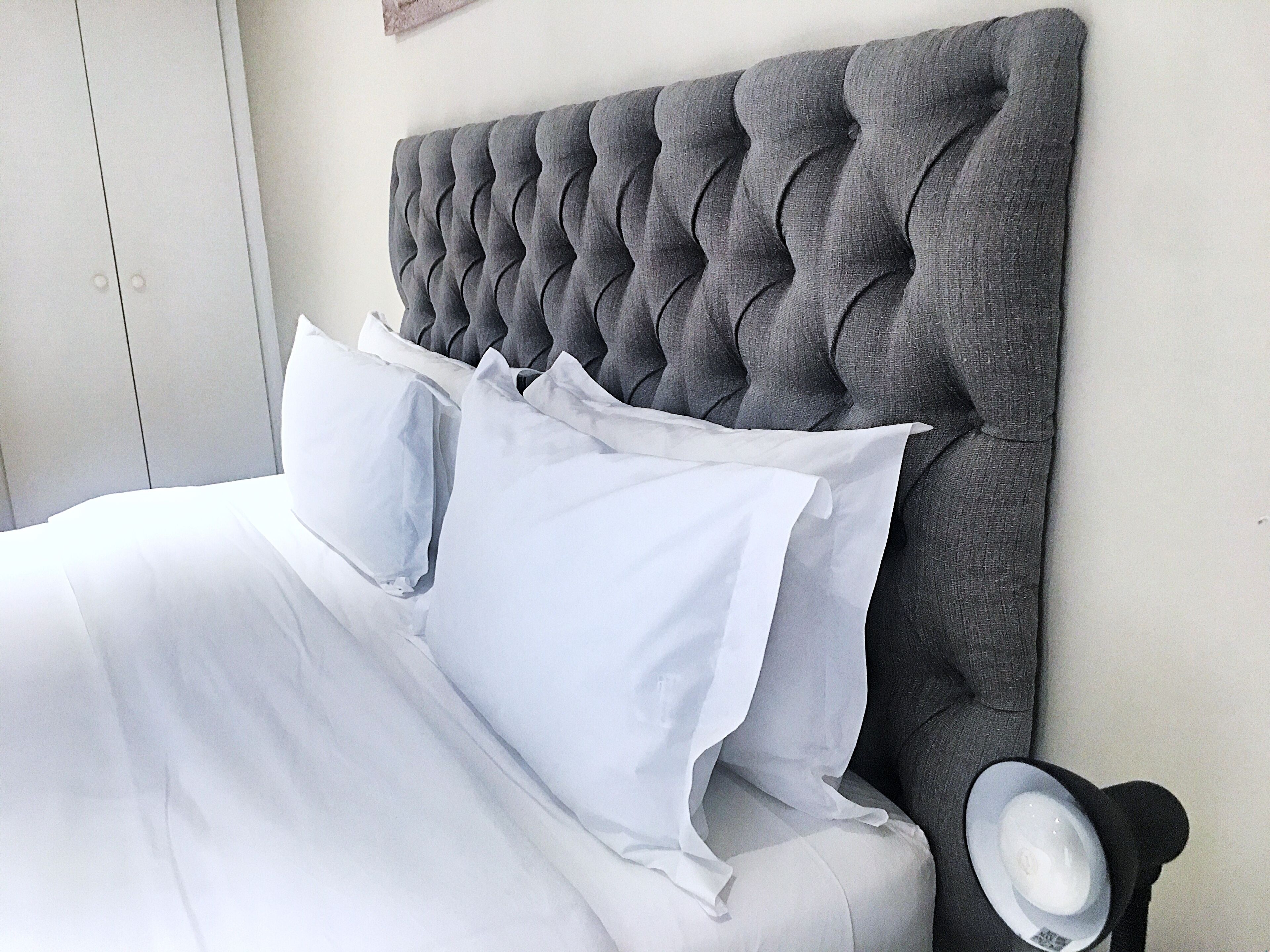 A bed with a tufted headboard, white bedding, and a bedside lamp.