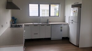 A modern kitchen with white cabinets, a built-in dishwasher, a stove, and a large window providing natural light. - Atiamuri Bach Family (Atiamuri)