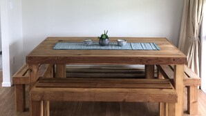 A wooden dining table with benches, a hanging white pendant light, and a framed landscape painting on the wall. - Atiamuri Bach Family (Atiamuri)