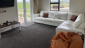 A living room with a white sofa, a television, and a large window with a view of a grassy field. - Atiamuri Bach Family (Atiamuri)