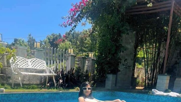 A person floating in a clear blue pool with a white chair and greenery in the background. - La Niebla Farm Resort (Ootacamund)