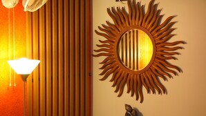 A room with a sun-shaped mirror, a standing lamp, and a small statue on a wooden cabinet. - La Niebla Farm Resort (Ootacamund)