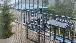 A balcony with a metal railing, a potted plant, and a view of a mountain in the background. - La Niebla Farm Resort (Ootacamund)