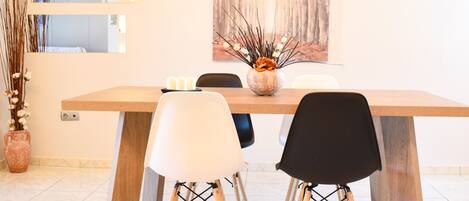 A dining area with a wooden table, four chairs, a vase with dried plants, and a large abstract painting on the wall.