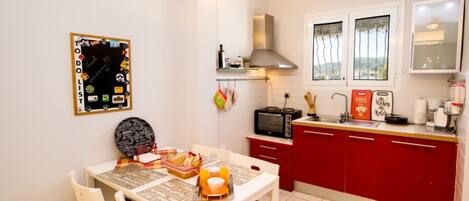 A compact kitchen with a red cabinet, a stove, and a microwave. There is a dining table with chairs and a basket of bread.